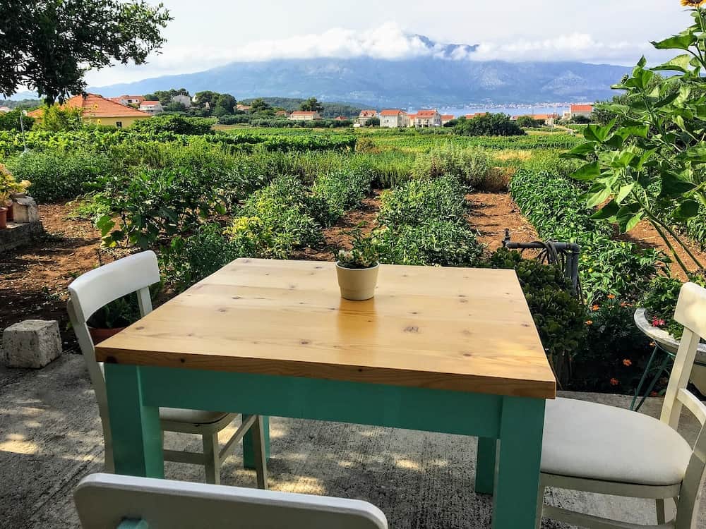 A table for a place to have dinner beside a sprawling wine vineyard growing the local grk grapes with the small town of Lumbarda in the background, on Korcula island in Croatia.
