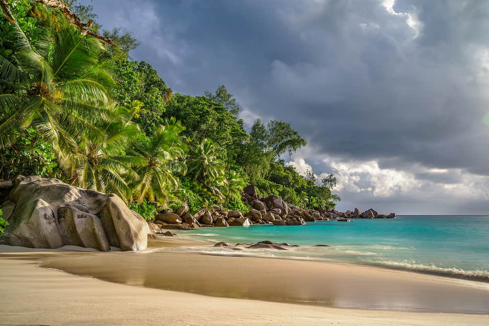 An approaching thunderstorm over the paradise. the sun shines bright under the black clouds and lightens up the palms, the granite rocks and the turquoise water of this beautiful dream beach at anse georgette on the seychelles