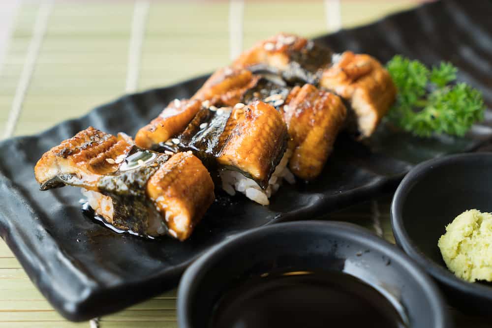 Unagi sushi on black plate along with Japanese sauce and green leaf decoration, Japanese food, close up at sushi.