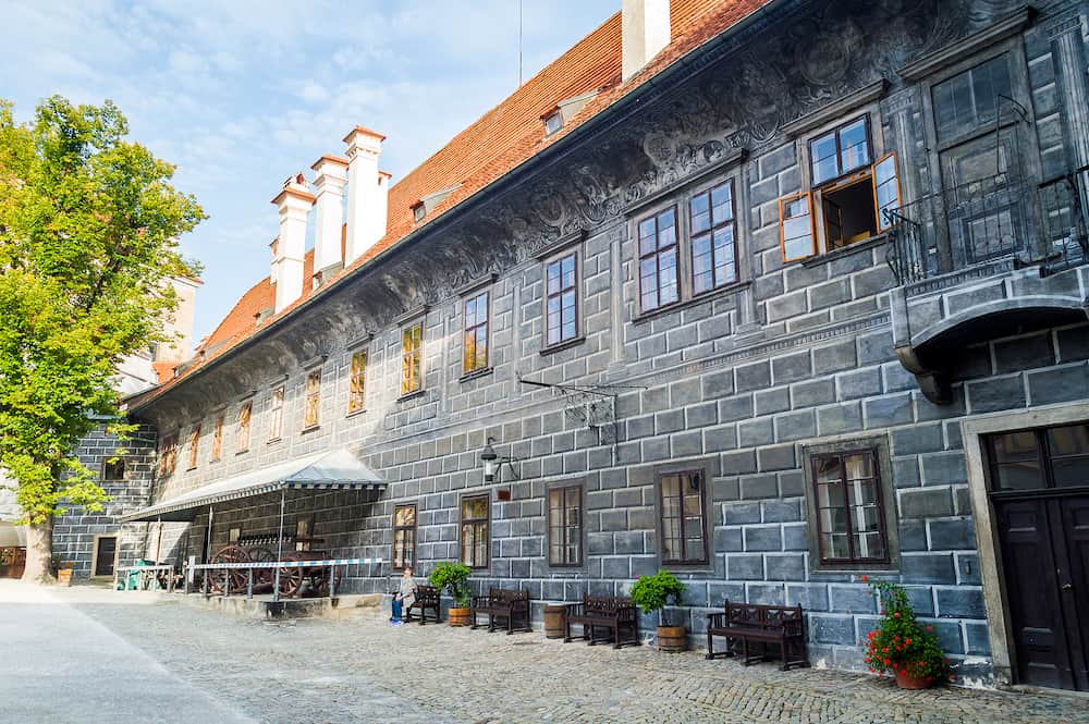 Fragment of wall and corner of Cesky krumlov castle in public courtyard with windows bench and flowers in pots