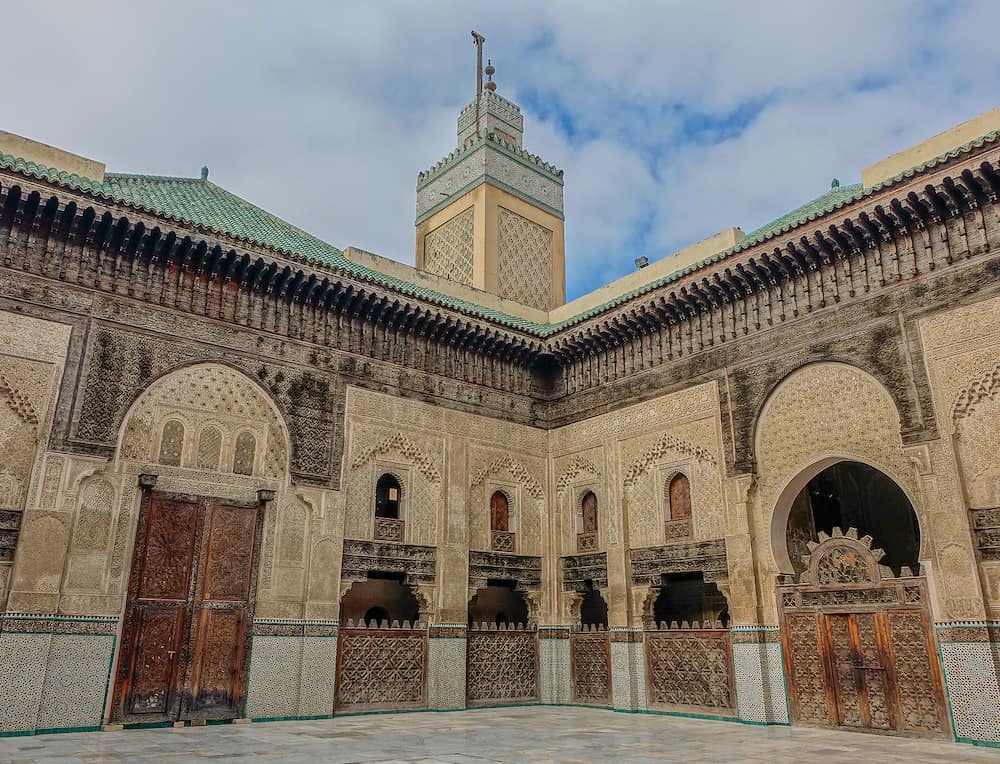 Fez, Morocco, Africa - Interior courtyard and minaret of the Al-Attarine Madrasa in Fez under a blue sky