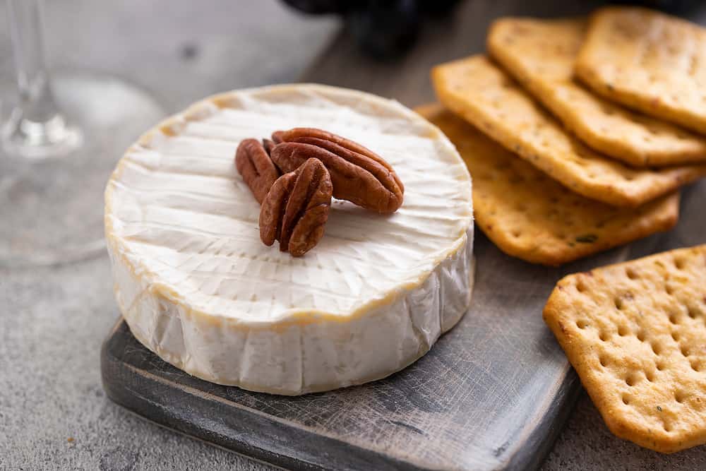French cheese on wooden board with crackers, perfect snack for red wine. Cheeseboard background.