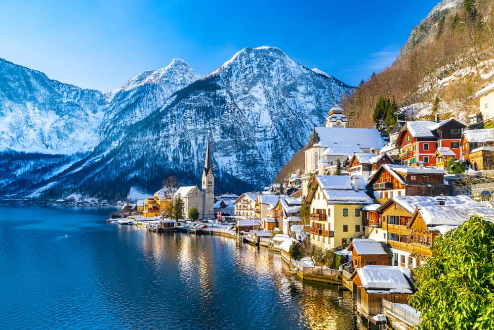 Classic postcard view of famous Hallstatt lakeside town in the Alps with traditional passenger ship on a beautiful cold sunny day with blue sky and clouds in winter, Austria