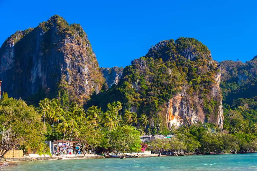 Tropical promenade embankment in a resort location on the background of high palm trees and limestone rocky mountains in clear bright windy weather. Floating Pier on Railay peninsula, Krabi, Thailand.