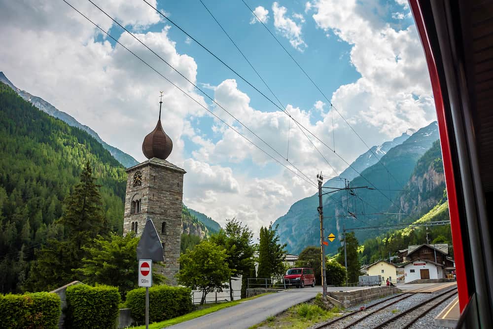 View of Pfarrkirche St.Niklaus with forest and mountains on background from panoramic train. Station St.Niklaus in canton of Valais.