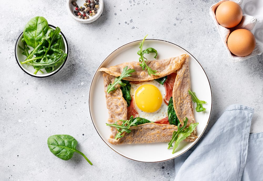 french buckwheat crepe with egg, ham and spinach on gray background. galette bretonne. flat lay.