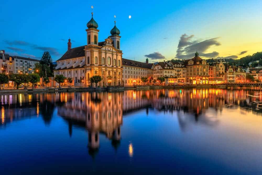 Blue twilight on Lake Lucerne in Switzerland. Jesuitenkirche Church of St. Francis Xavier reflects on Reuss river of Lucerne town. Reflections of Lucerne cathedral on the river at night.