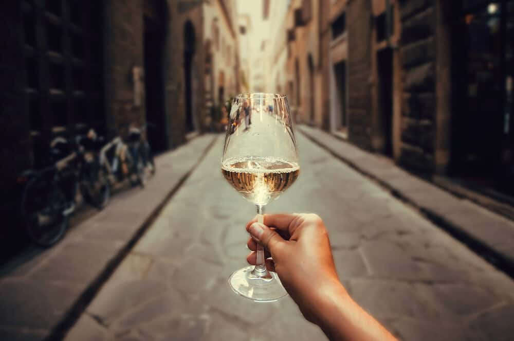 Happy tourist walking on narrow streets with white wine glass in hand. Enjoying life concept.