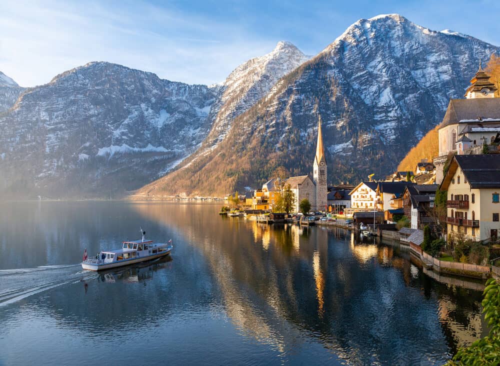 VIew of beautiful Hallstatt lake and famous church during morning sunrise in early spring, tour boat coming in