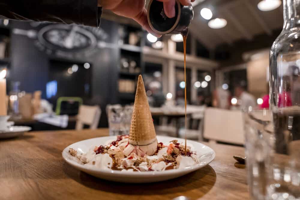 Man pouring caramel over delicious ice cream dessert on table at restaurant