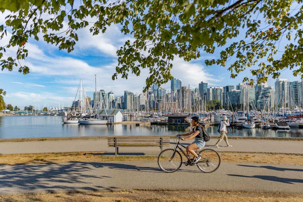 Vancouver, British Columbia, Canada in summer day. Unidentified tourists and bicyclists at Stanley Park and Vancouver Skyline with marina