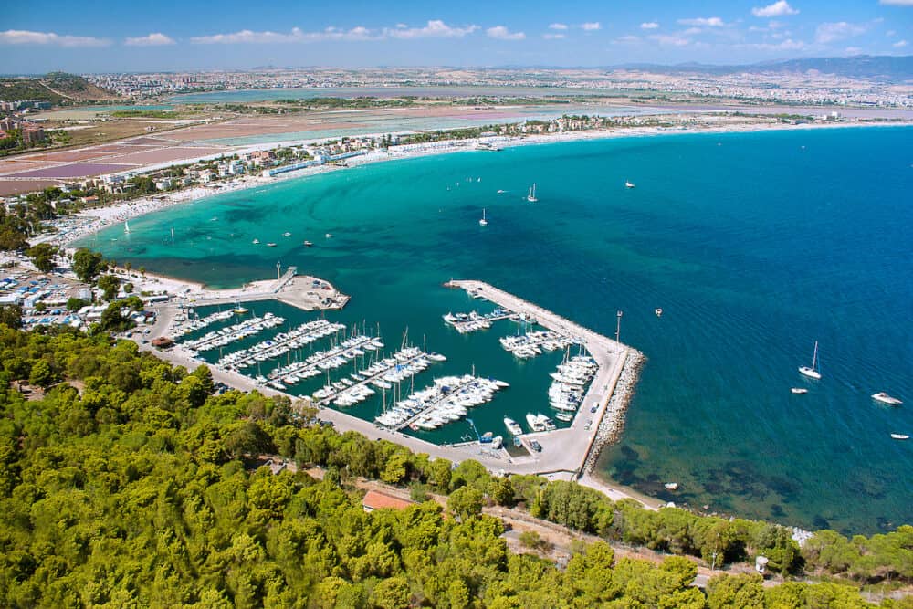 Areal view on Cagliari with green forest a port with boats famous beach Il Poetto and mountains in Sardinia Italy.