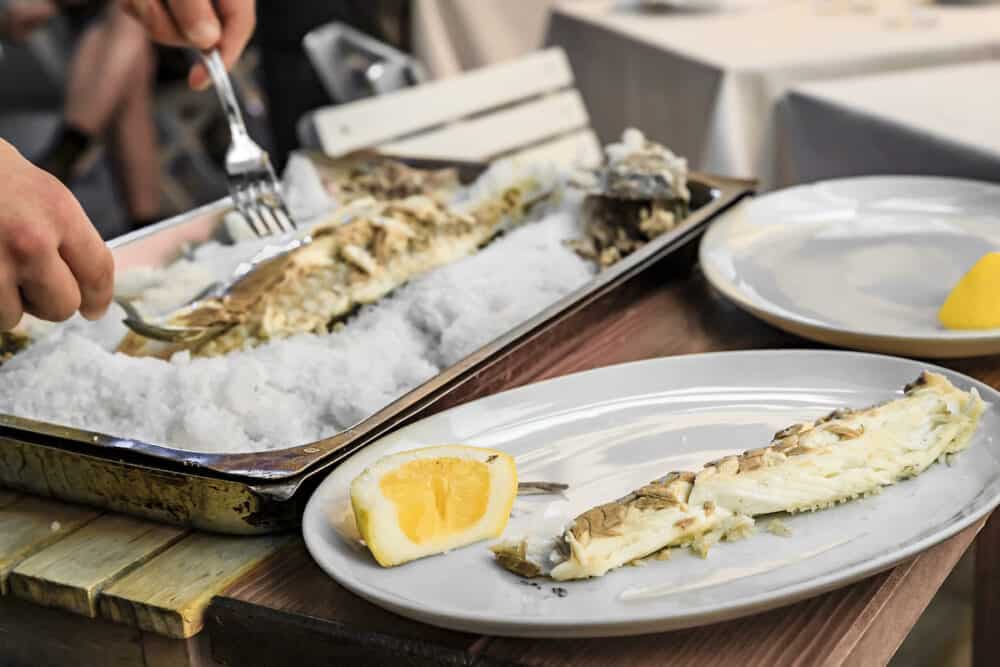 Branzino or Mediterranean sea bass whole roasted in salt fish filleted at the table by a waiter at a street restaurant in Vernazza, Cinque Terre Italy