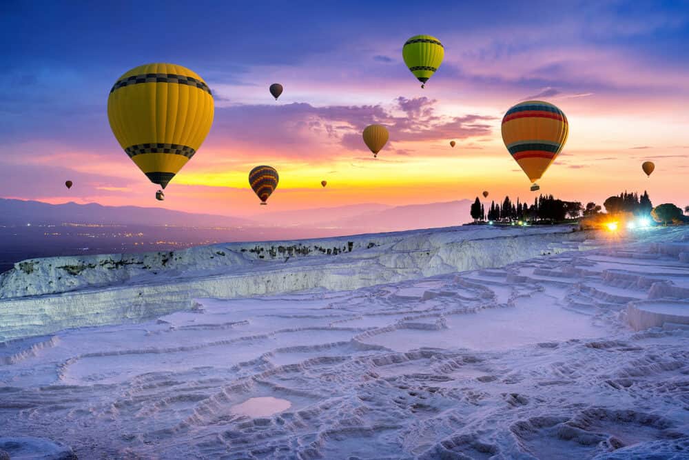Hot air balloons and Natural travertine pools at sunset in Pamukkale, Turkey.