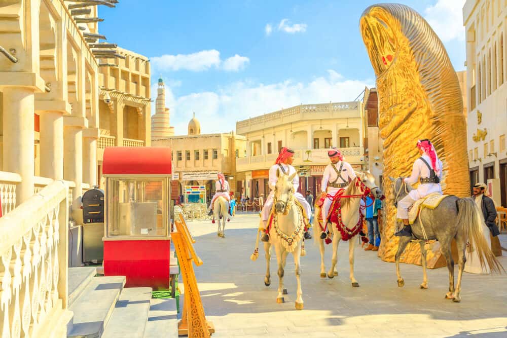 Doha, Qatar - police officers, famous attraction, riding white Arabian horses at Souq Waqif. Fanar Islamic Cultural Center with Mosque and golden giant thumb sculpture on background