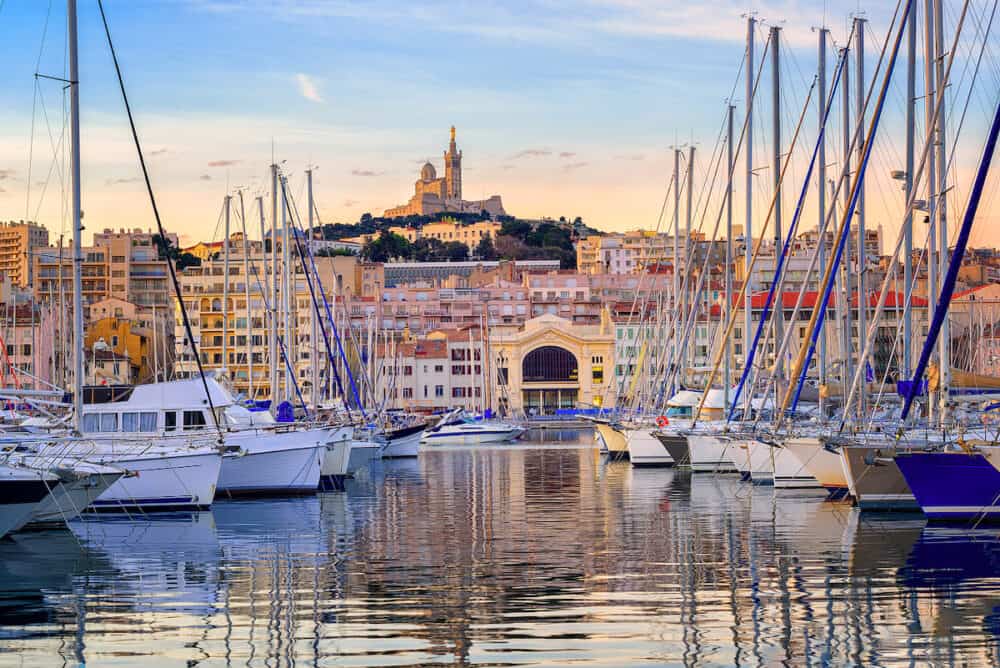 Yachts reflecting in the still water of the old Vieux Port of Marseilles beneath Cathedral of Notre Dame France on sunrise