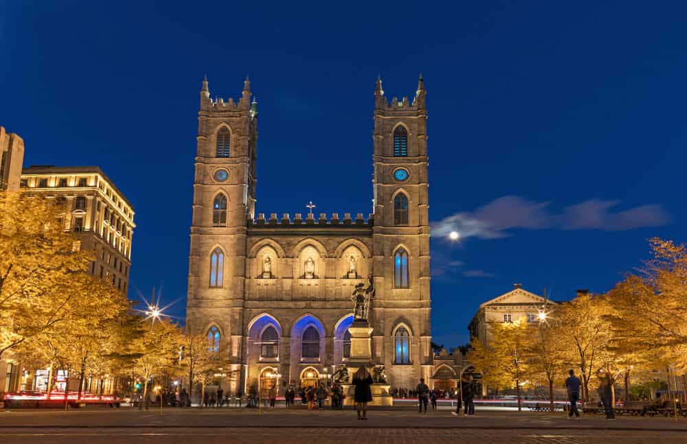 Montreal, Canada. Notre Dame Basilica from Montreal and Maisonneuve Monument illuminated at night time, during autumn season.  First neo-gothic church in Canada.