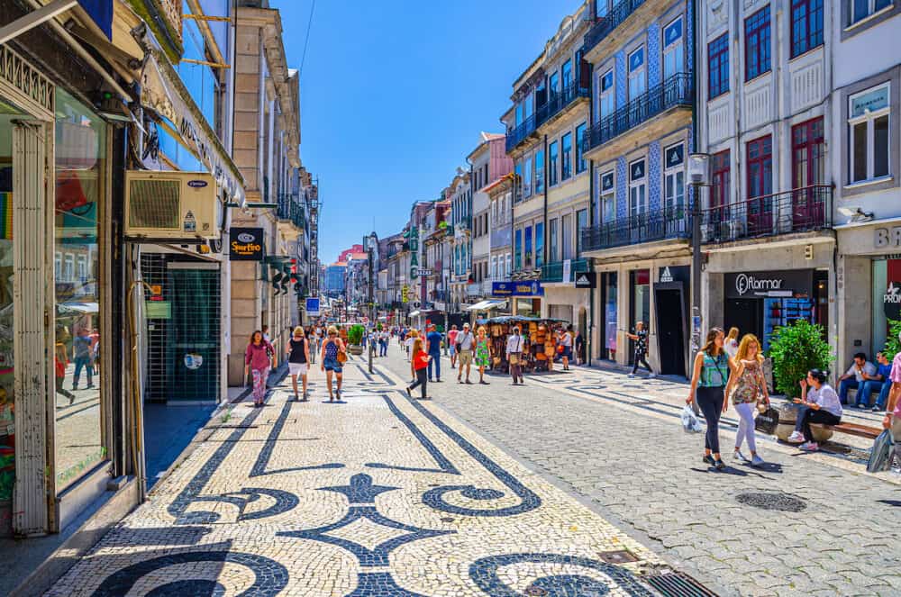 Porto, Portugal - people tourists walking down Rua de Santa Catarina cobblestone pedestrian street with colorful buildings and houses in historical city centre in sunny summer day
