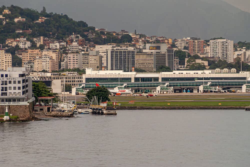 Rio de Janeiro, Brazil - Airport field and LATAM plane with tall buildings of Centro district behind. Guanabara bay water in front.