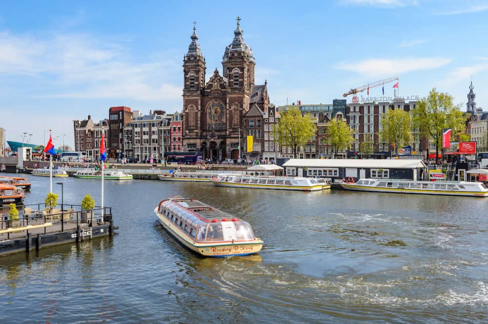 Amsterdam, Netherlands -  Tourists sightseeng at Canal Boats near the Central Station of Amsterdam. View to Basilica of Saint Nicholas