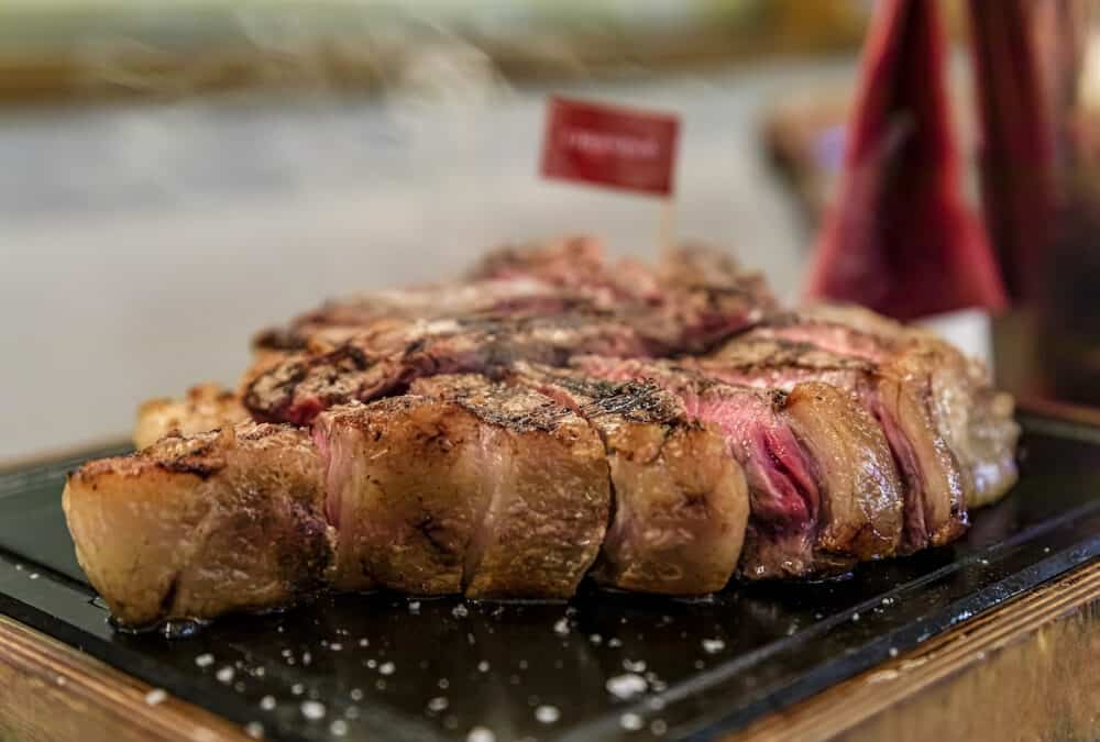 Classic seared dry aged T-bone Florentine steak from a Chianina cow steaming on a grill serving plate at a restaurant in Florence, Italy
