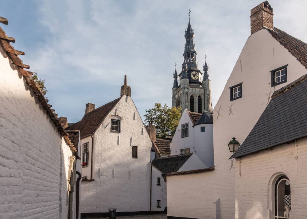 Kortrijk, Flanders, Belgium -  Spire of Notre Dame church seen from Corner of beguinage with white and red roofed housing. Some green foliage.