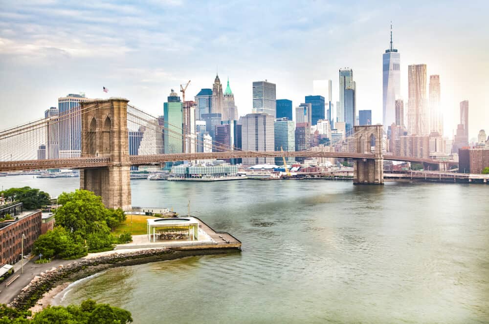Amazing view of New York city skyline and Brooklyn bridge with skyscrapers and East River flowing during daytime in United States of America