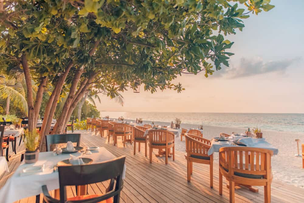 Outdoor restaurant at the beach. Table setting at tropical beach restaurant. Sunset scenery, amazing sky and beach, luxury mood