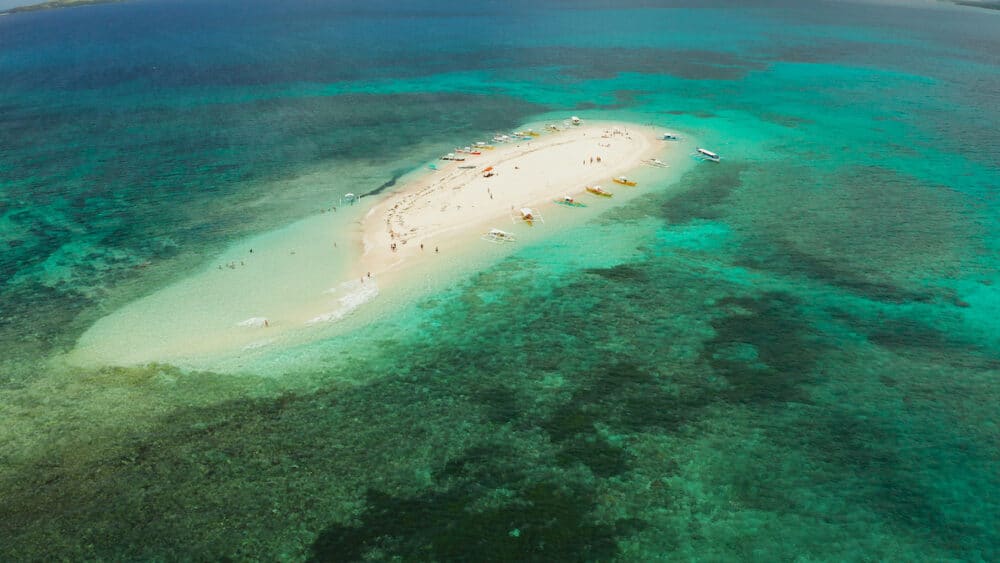 Sandy white island with beach and sandy bar in the turquoise atoll water, aerial drone. Tropical island and coral reef. Naked Island, Siargao.