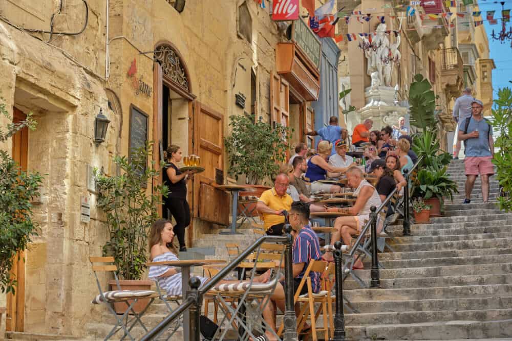 Valletta, Malta - Tourists enjoy a break on the steps of the St. Lucia Street