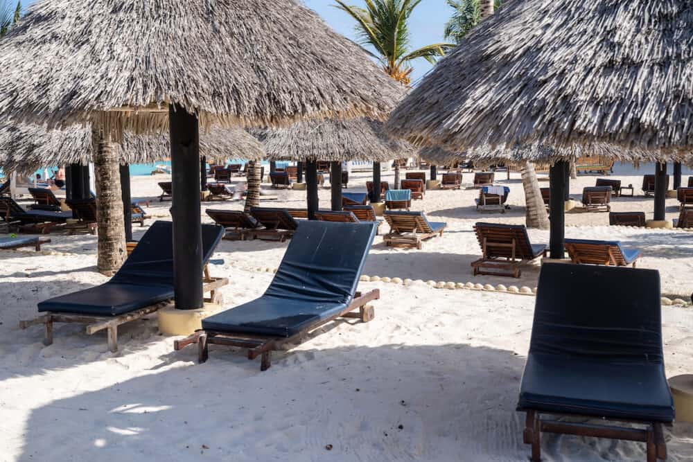 Chaise sun loungers with shaded thatched roof umbrellas at a resort in Zanzibar, Tanzania for tanning on the beach