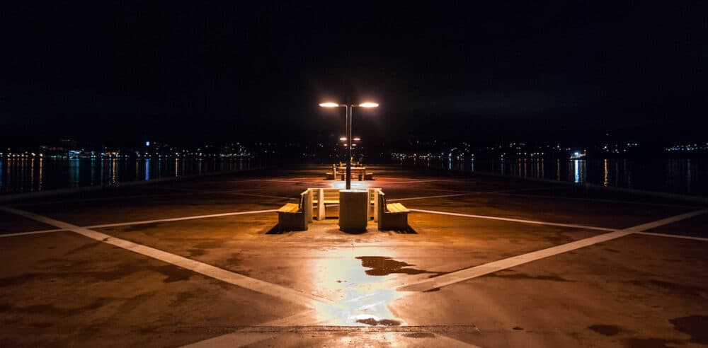 Empty benches and energized lights on a Halifax, Nova Scotia night.  Long Jetty protrudes into the harbor.  City of Halifax at night.
