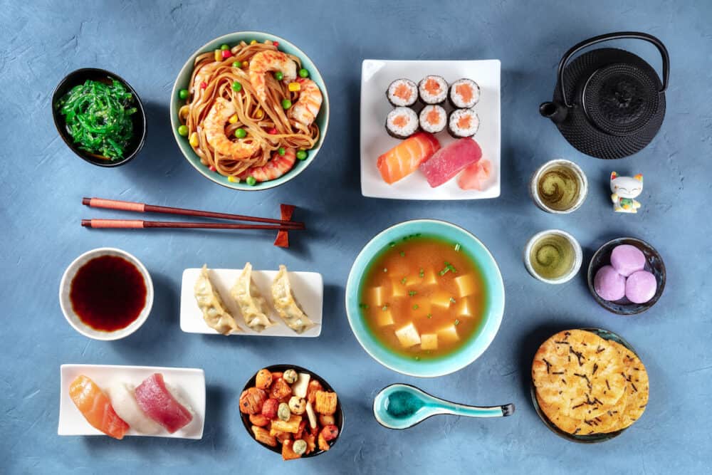 Japanese Food, Sushi, udon, miso soup, tea, mochi , overhead flat lay shot on a blue background