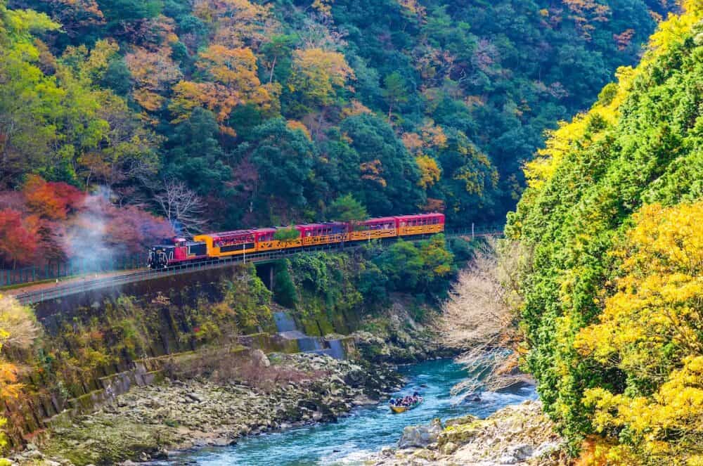 beautiful mountain view in colorful autumn season with sagano scenic railway or romantic train on bridge and boat in the river in Arashiyama, Kyoyo, Japan