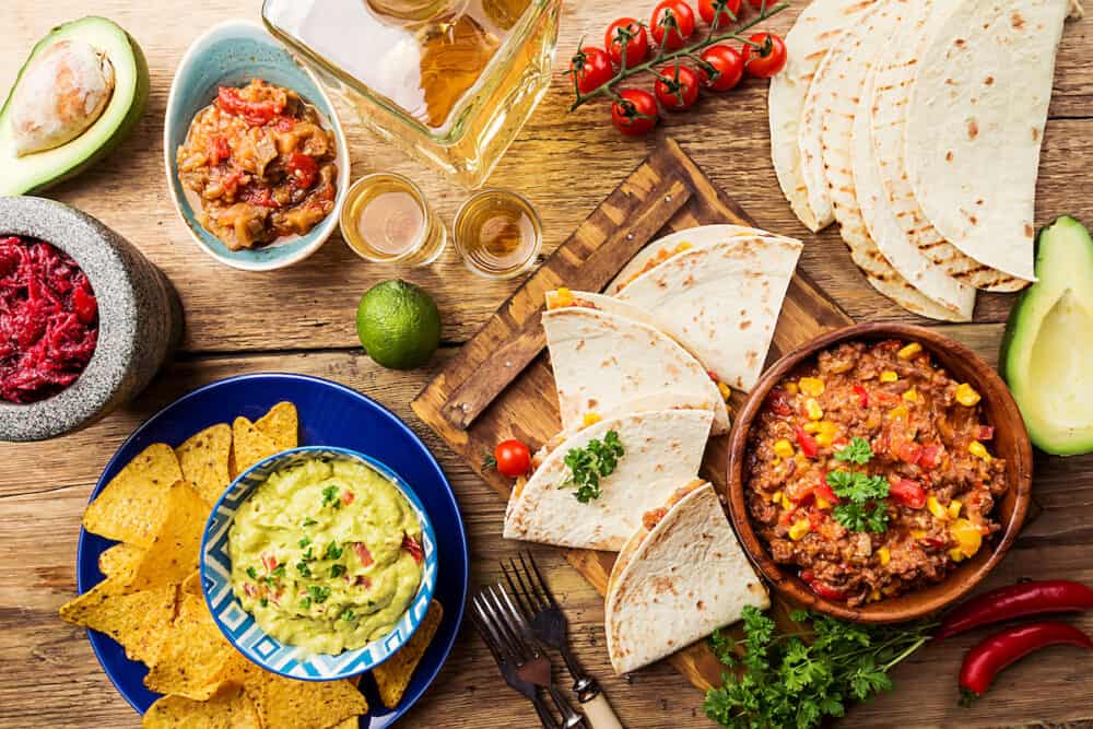 Mexican food mix: nachos, fajitas, tortilla, guacamole and salsa sauces and ingredients over wooden background. Top view