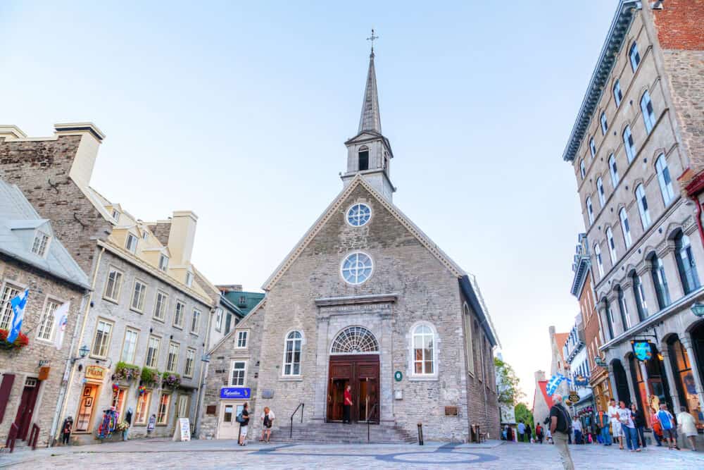 QUEBEC CITY, CANADA - Tourists meander the cobblestone streets of Place Royale in Old Quebec city, in front of Notre-Dame-des-Victoires (Our Lady of Victories) Church erected in 1688, the oldest stone church in North America.