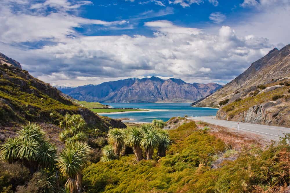 Beatiul blue Hawea lake near town of Wanaka in New Zealand, highway picture of New Zealands mountain landscape, road trip in New Zealand, popular travel destination