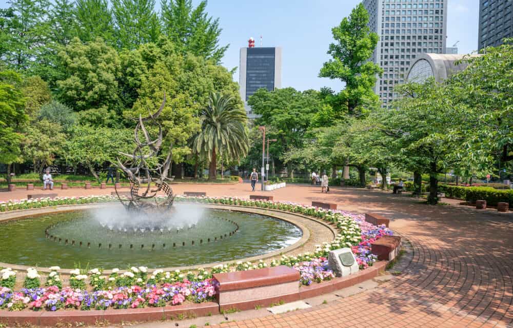 Tokyo, Japan -  Fountain and trees in the Hibiya Park in Tokyo city center with skyscrapers in the background on a warm sunny day of spring