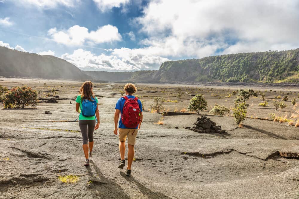 Couple tourists hikers walking on Kilauea Iki crater trail hike in Big Island, Hawaii. USA summer travel vacation destination for outdoor nature adventure, american tourism.