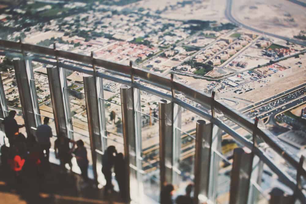 True tilt shift shooting of observation deck of Burj Khalifa skyscraper with group of people observing Dubai from top: highway sand areas residential buildings and streets