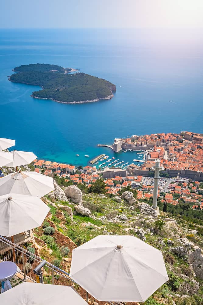 Umbrellas providing shadow for restaurant customers on top of a Srd Hill with the view of the old city of Dubrovnik, on the UNESCO list of World heritage site, Croatia.