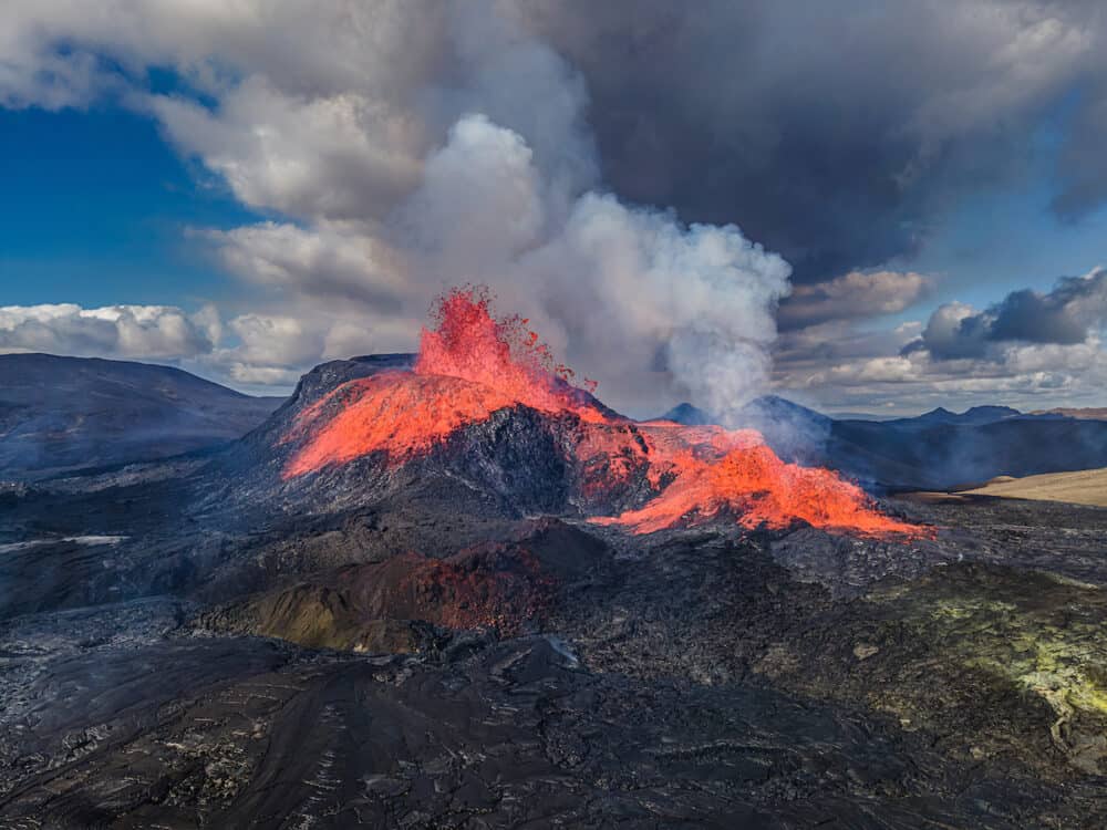 Aerial view of the crater opening from Fagradalsfjall volcano. Crater with strong lava flow on Iceland in the GeoPark. Daytime volcanic eruption on Reykjanes peninsula. Clouds and steam in the sky