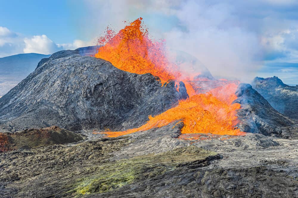 Eruption of an active volcano on the Reykjanes Peninsula. strong lava flow from a volcanic crater in Iceland. liquid magma from crater at day in sunshine with clouds and blue sky