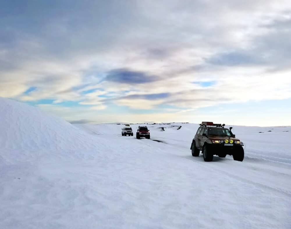 A caravan of Icelandic super jeeps off-roads in the snow while taking tourist to the famous ice cave tours, on a cloudy winter day.