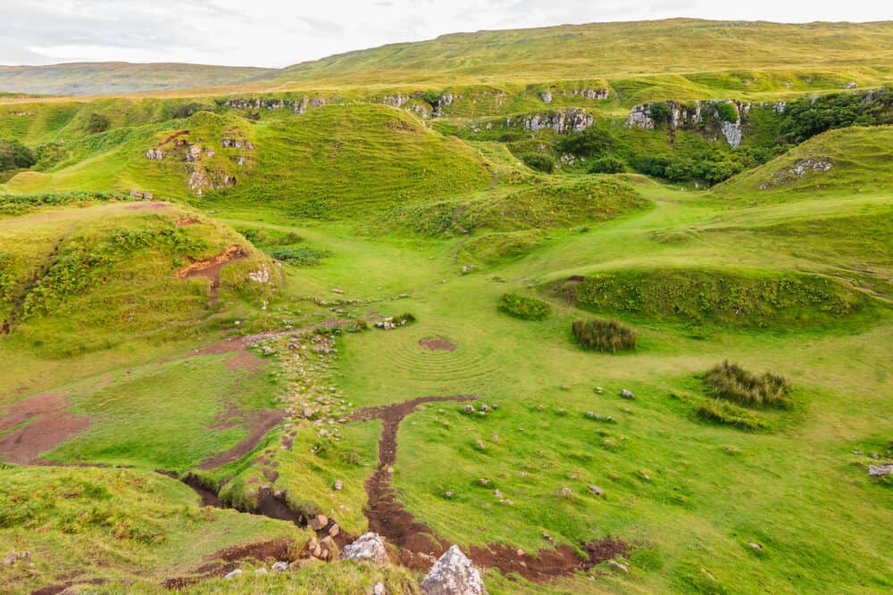 Landscape on the Isle of Skye in Scotland. Meadows of Fairy Glen with central circles on the green. Small hills with bushes and clouds in the sky. Well-trodden paths with earth in summer