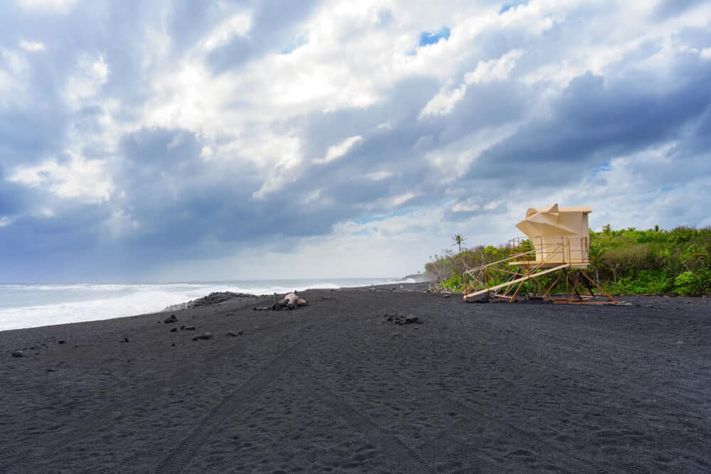 Lifeguard tower on a black sand beach, set against a dramatic sky over the ocean.