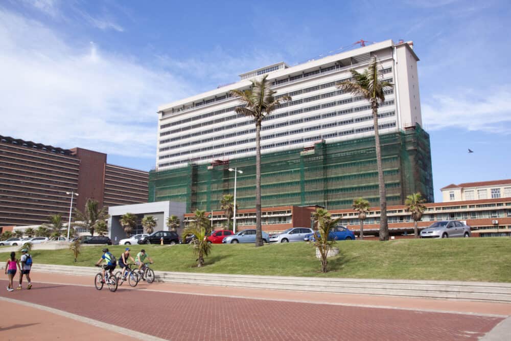 DURBAN SOUTH AFRICA - Four pedestrians and cyclists on promenade in front of refurbished Addington Hospital on Golden mile beachfront in Durban South Africa