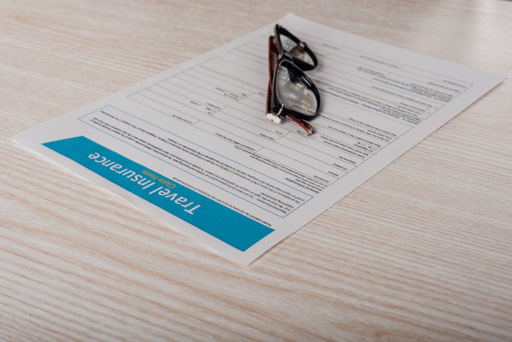 Travel insurance application form with glasses on wooden table