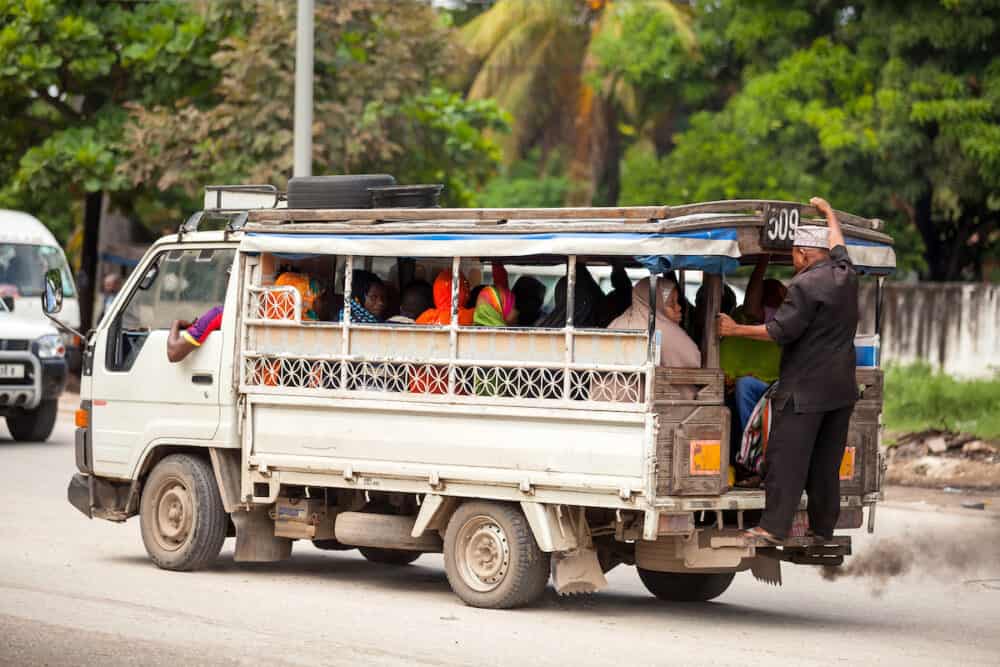 Stone Town, Zanzibar -  Taxi taking people to market. Man riding on back of taxi.
