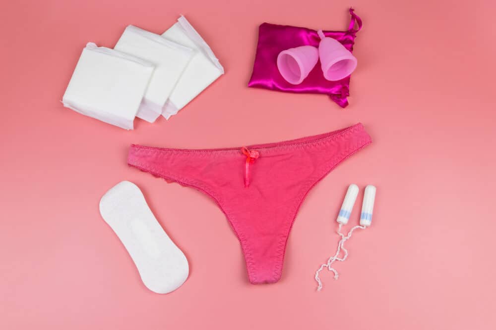 Women's panties with menstrual cups, sanitary pads and tampons on pastel pink background. Top view. Concept of critical days, menstruation, feminine hygiene